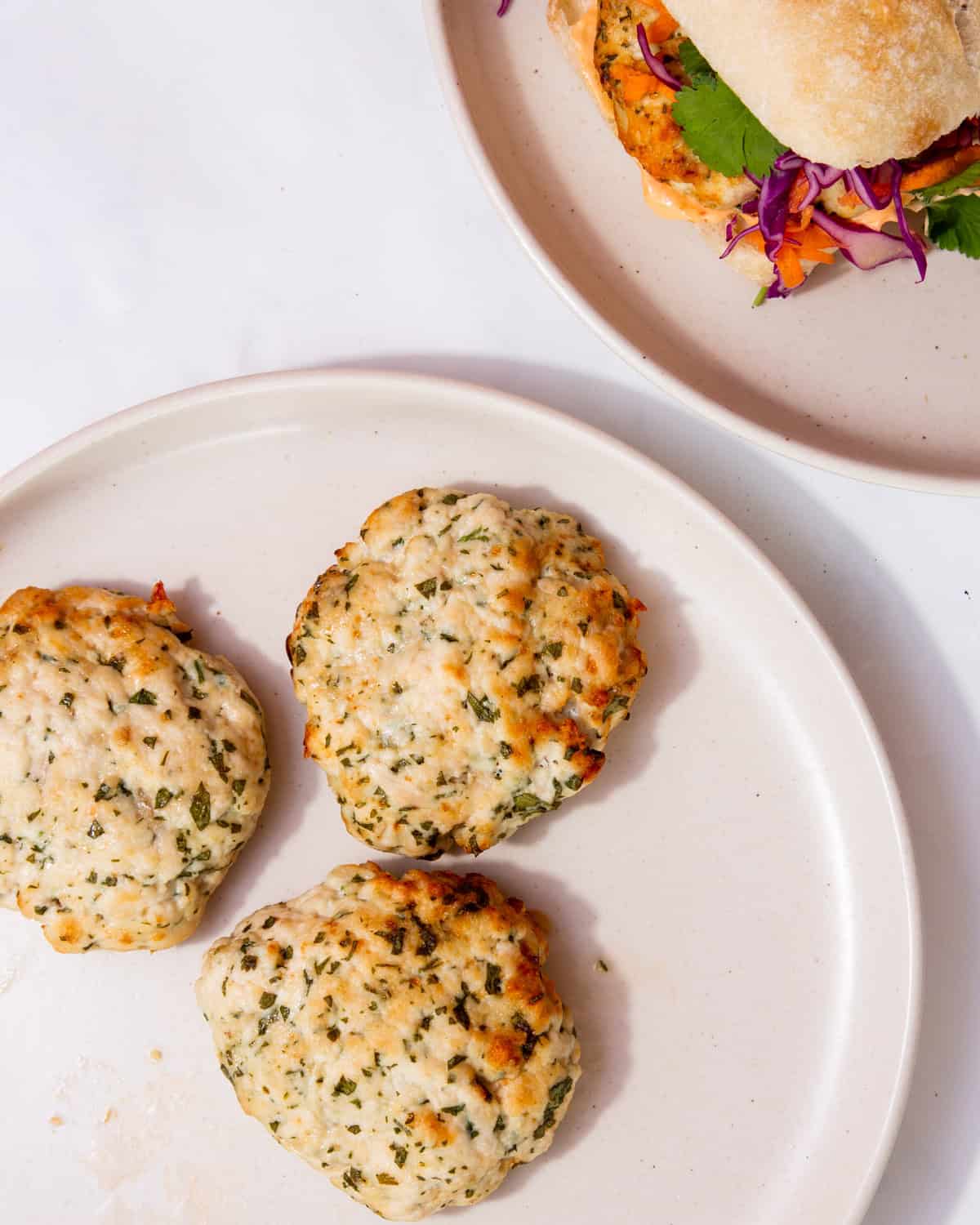 3 chicken patties on a plate next to another plate with the patties in a burger bun.