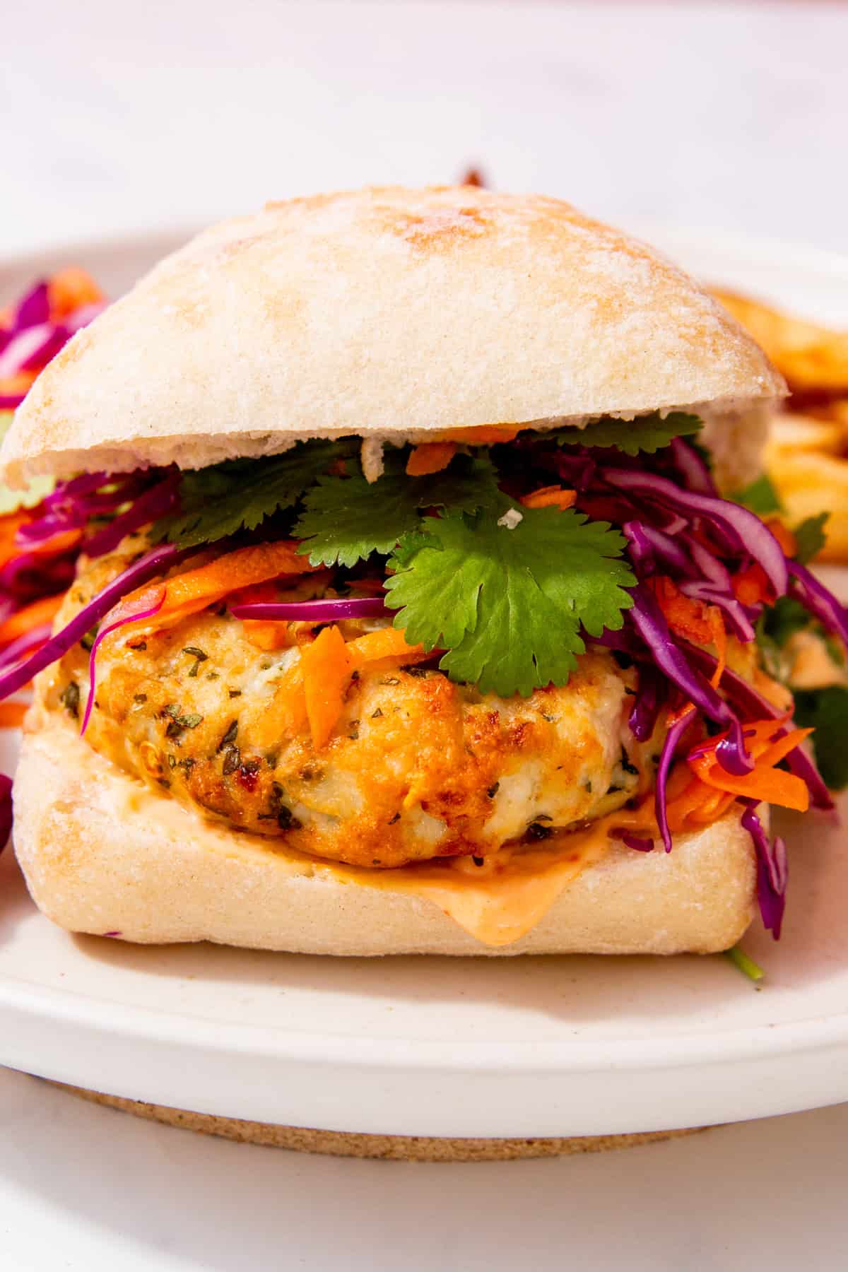 A burger bun filled with a chicken pattie and salad including red cabbage, coriander, carrot and cheese.