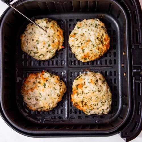 4 cooked and golden brown chicken patties in air fryer tray with a thermometer in one burger.