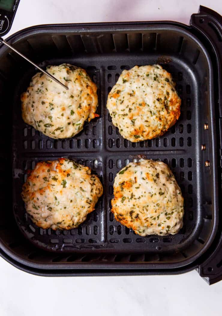 4 cooked and golden brown chicken patties in air fryer tray with a thermometer in one burger.