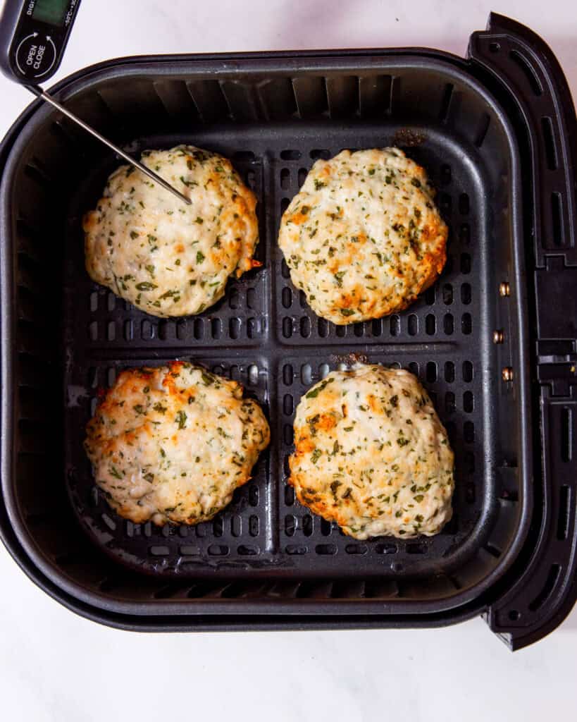 4 cooked and golden brown chicken patties in air fryer tray with a thermometer in one burger.