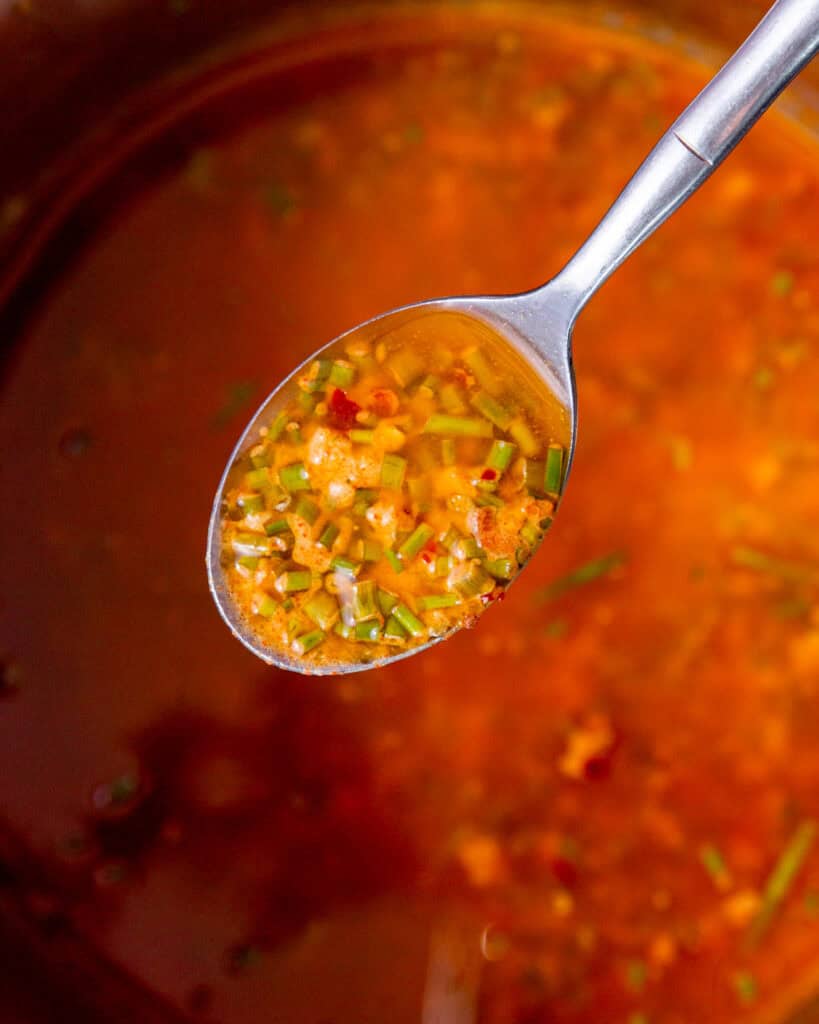 A spoon with melted butter and herbs over melted butter mix.