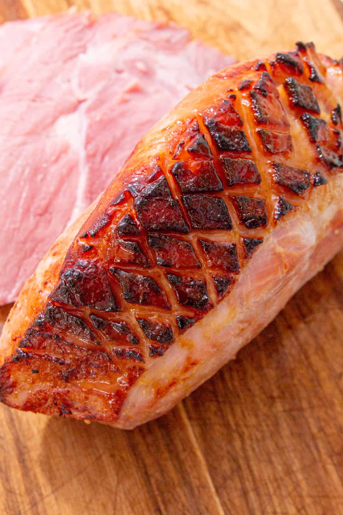 A large gammon joint with  the fat scored and browned with the cooked gammon joing on a wooden chopping board.