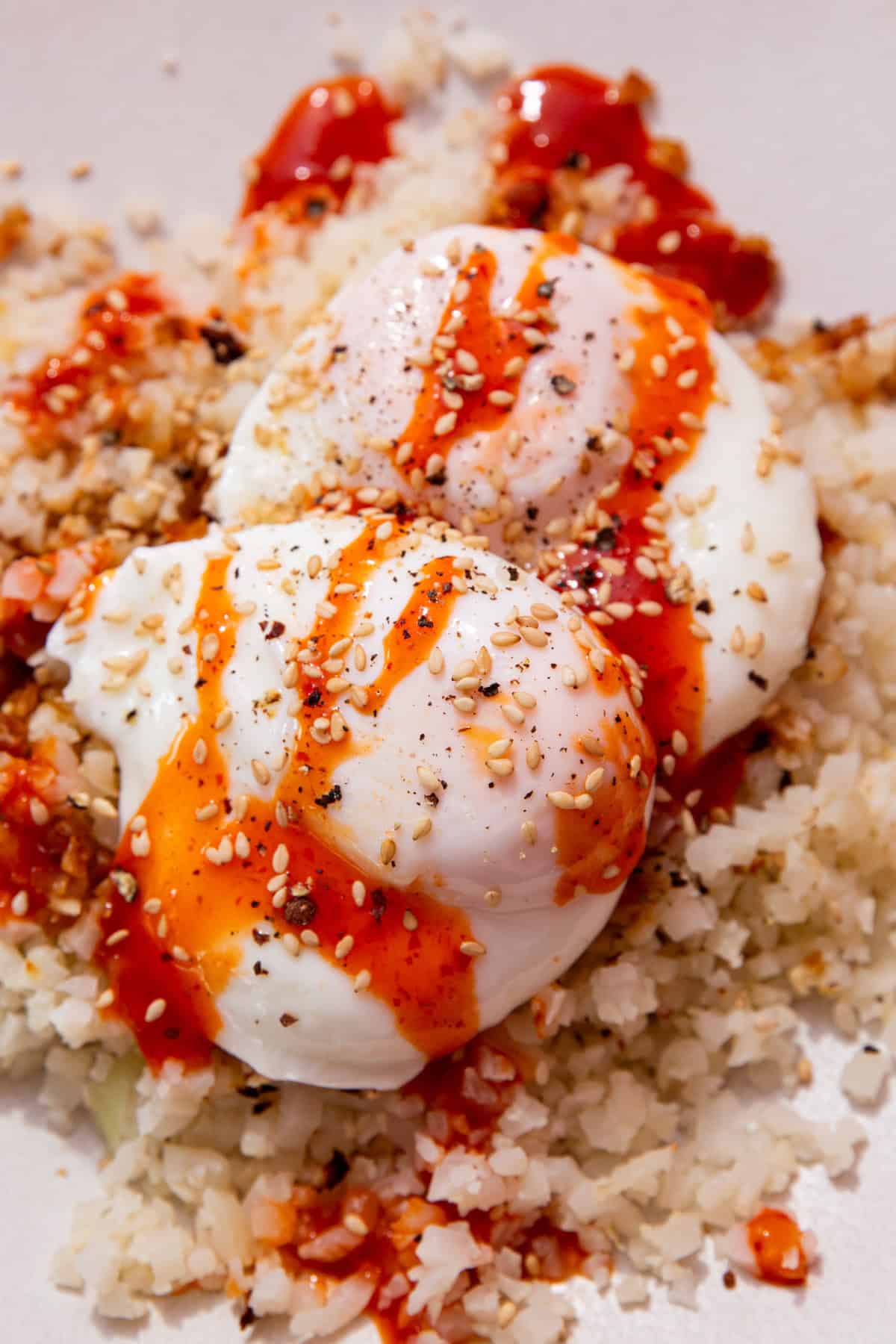 2 cooked poached eggs on a bed of rice with a drizzle of sriracha over the top.