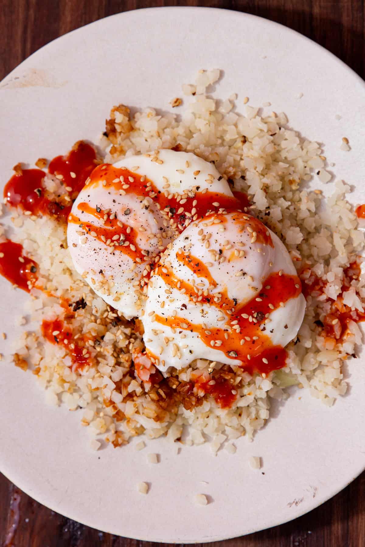 2 poached eggs on a bed of white rice with some brown seasoning and a drizzle of sriracha over the eggs.