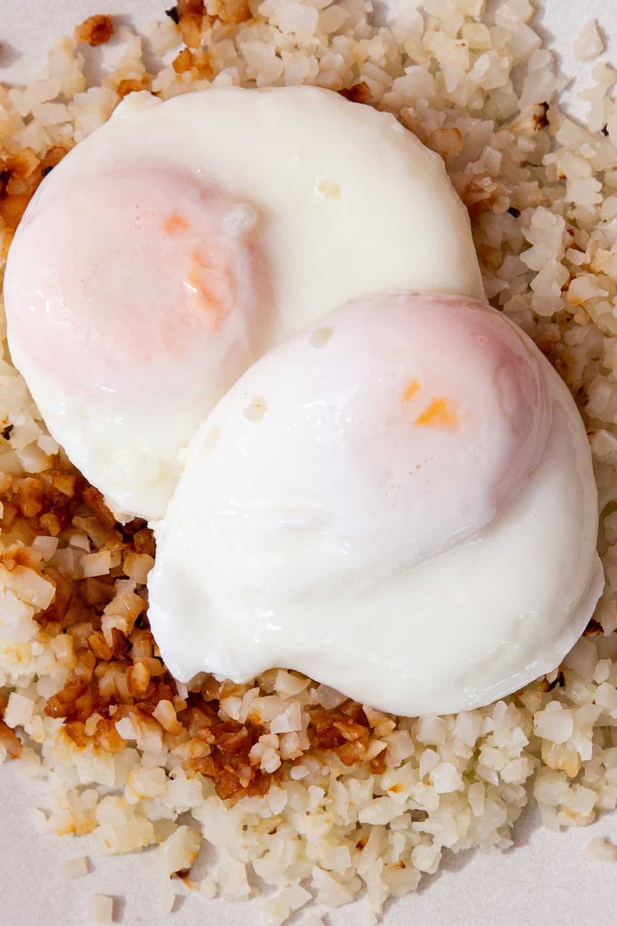 2 poached eggs on a bed of white rice with some brown seasoning.