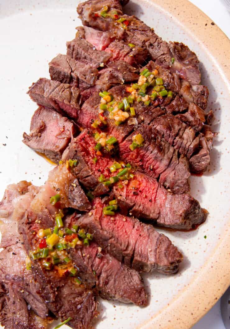 Slices of cooked rib eye steak, some medium rare slices in the middle and some dressing poured overdrizzled over the middle of the steak slices