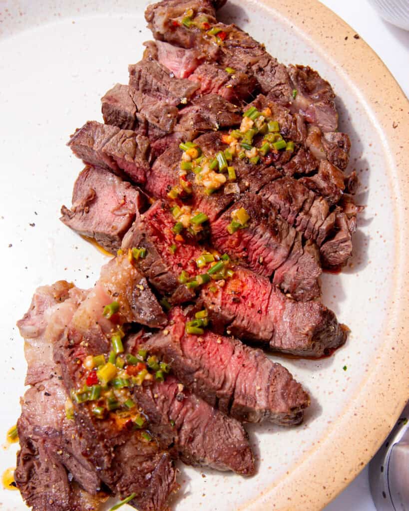 Slices of cooked rib eye steak, some medium rare slices in the middle and some dressing poured overdrizzled over the middle of the steak slices