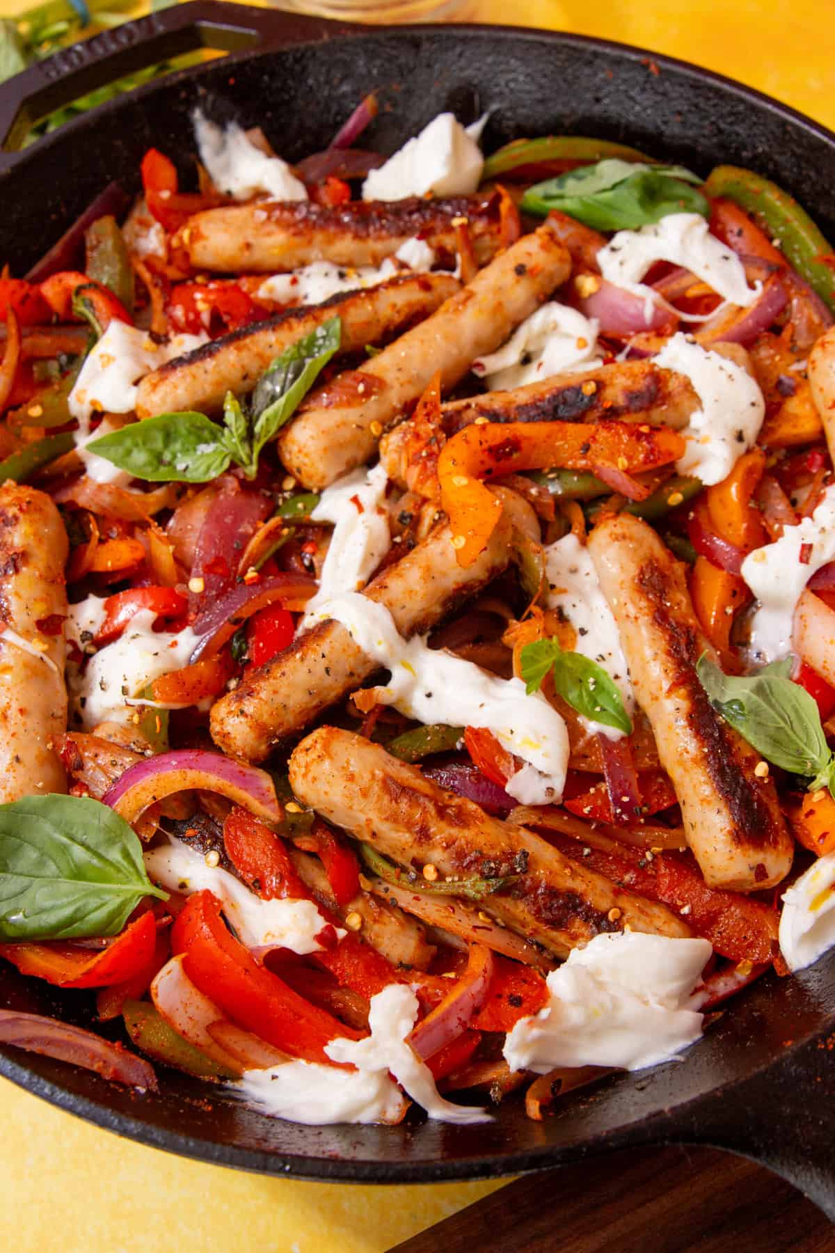 Golden browned sausages, peppers, onion and mozarella cheese topped with fresh basil in a skillet pan.