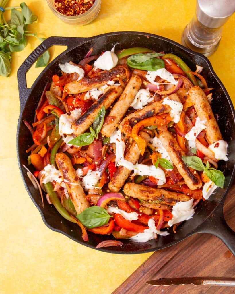 A harge skillet pan with Golden browned sausages, peppers, onion and mozarella cheese topped with fresh basil.