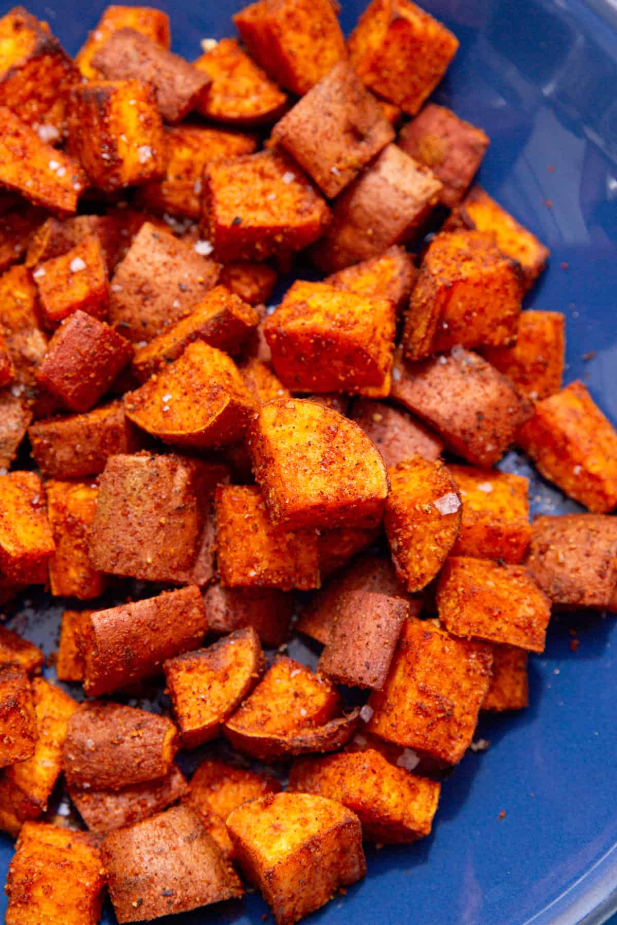 Lots of cooked and browned sweet potato cubes on a blue plate.