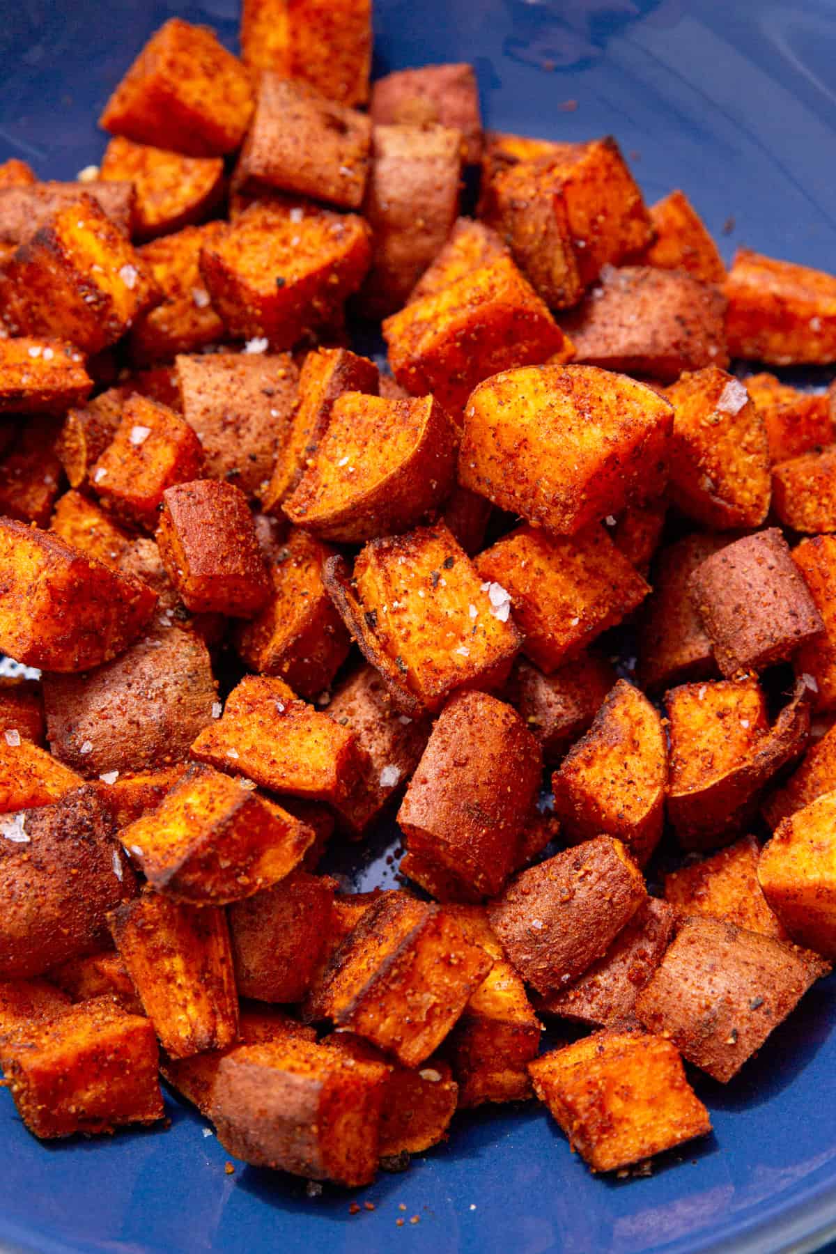 Lots of cooked and browned sweet potato cubes on a blue plate with some sea salt sprinkled over.