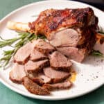 feature image of air fryer leg of lamb laying on a white plate with a sprig of rosemary and slices of lamb