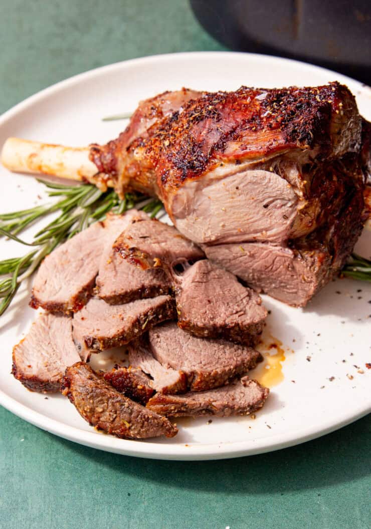 feature image of air fryer leg of lamb laying on a white plate with a sprig of rosemary and slices of lamb