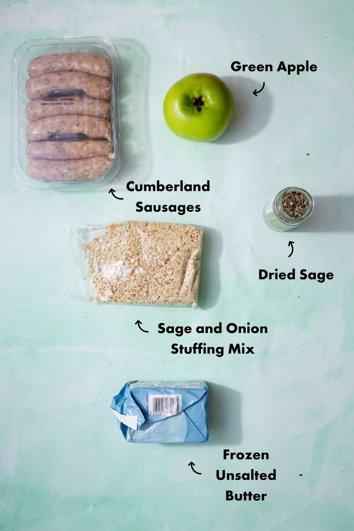 Ingredients to make the sausage meat stuffing in the oven laid out on a pale blue-green background and labeled with arrows.