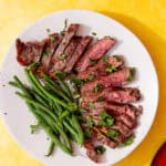 frozen steak in air fryer feature image of perfectly cooked steak that has been sliced and fanned around a white plate next to green beans and sprinkled with parsley