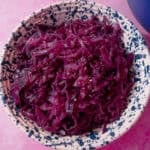 braised red cabbage in a blue and white speckled bowl on a purple background