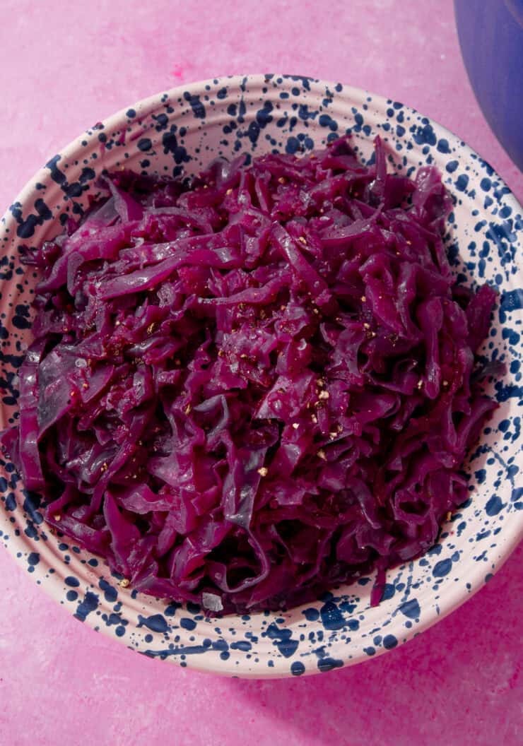 braised red cabbage in a blue and white speckled bowl on a purple background