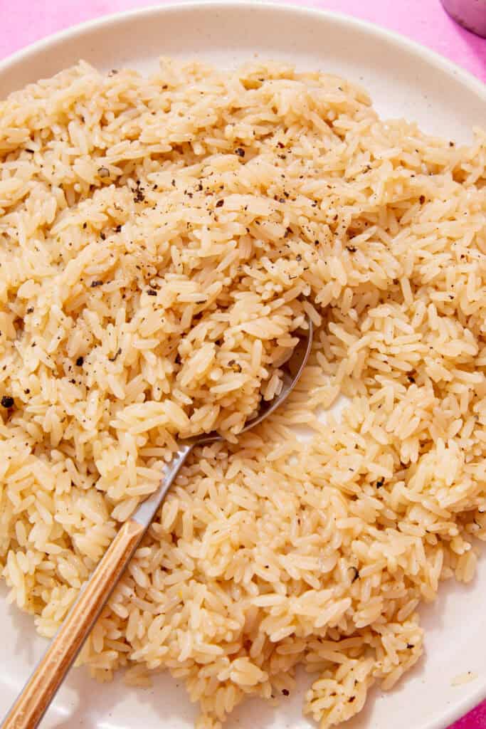 close up photo of fluffy seasoned rice with chicken broth and butter on a white plate with a spoon.