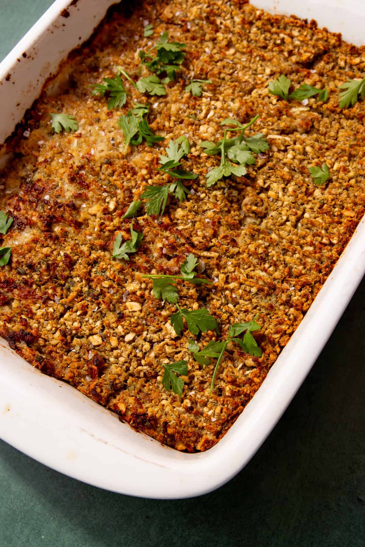 close up of sausage meat stuffing after baking with a browned top and parsley on top in a white baking dish.