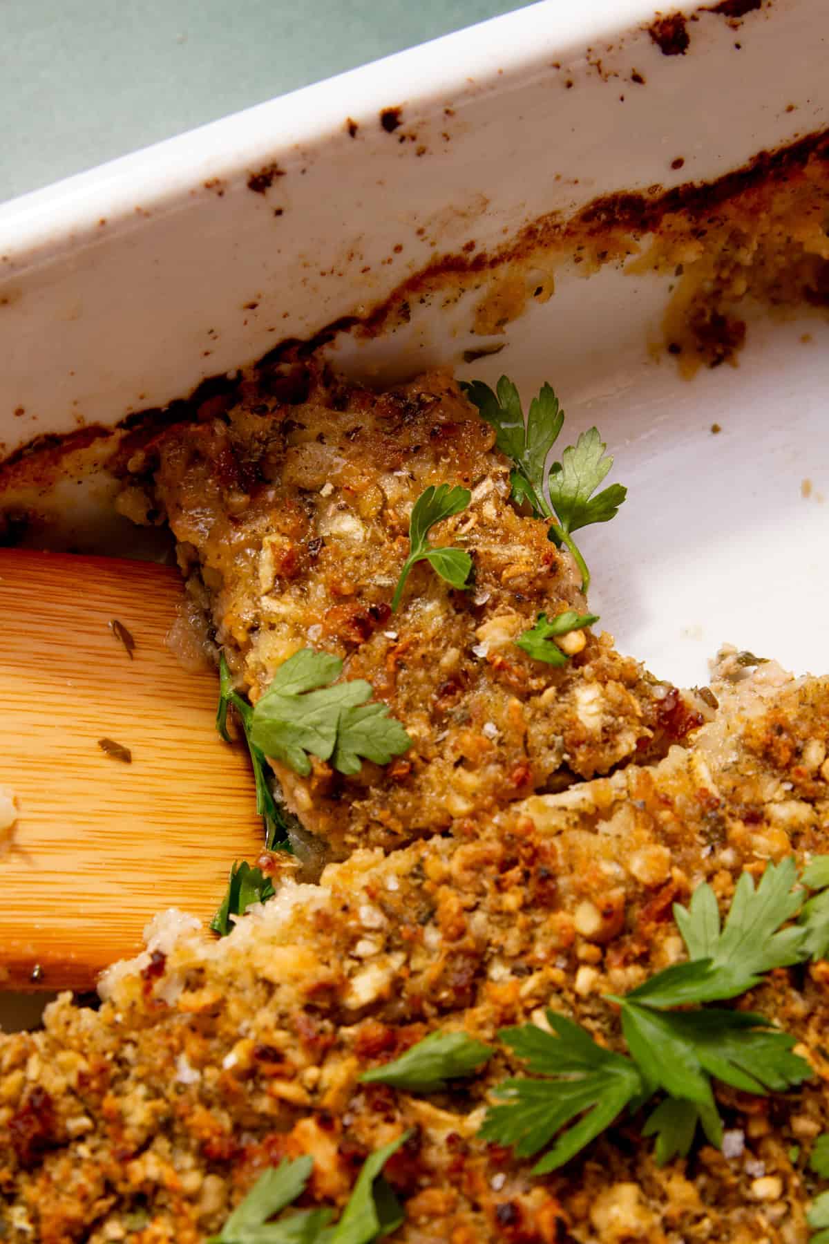 a slice of sausage meat stuffing being removed from a white dish with a wooden spatula.