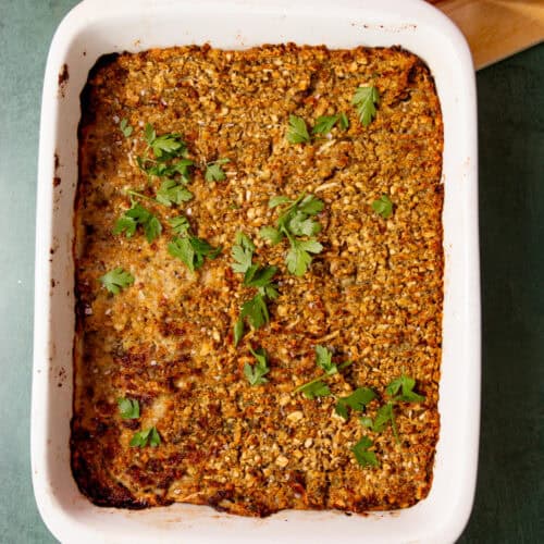 Baked sausage meat stuffing with a browned top and sprinkled with parsley in a white baking dish on a light green background