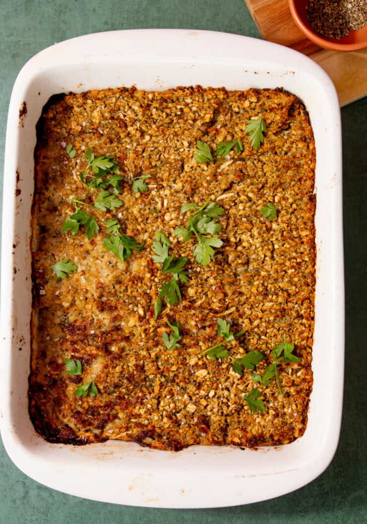 Baked sausage meat stuffing with a browned top and sprinkled with parsley in a white baking dish on a light green background