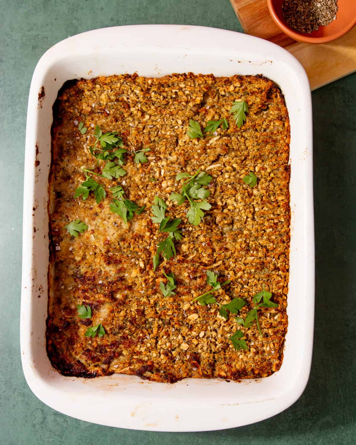 Baked sausage meat stuffing with a browned top and sprinkled with parsley in a white baking dish on a light green background