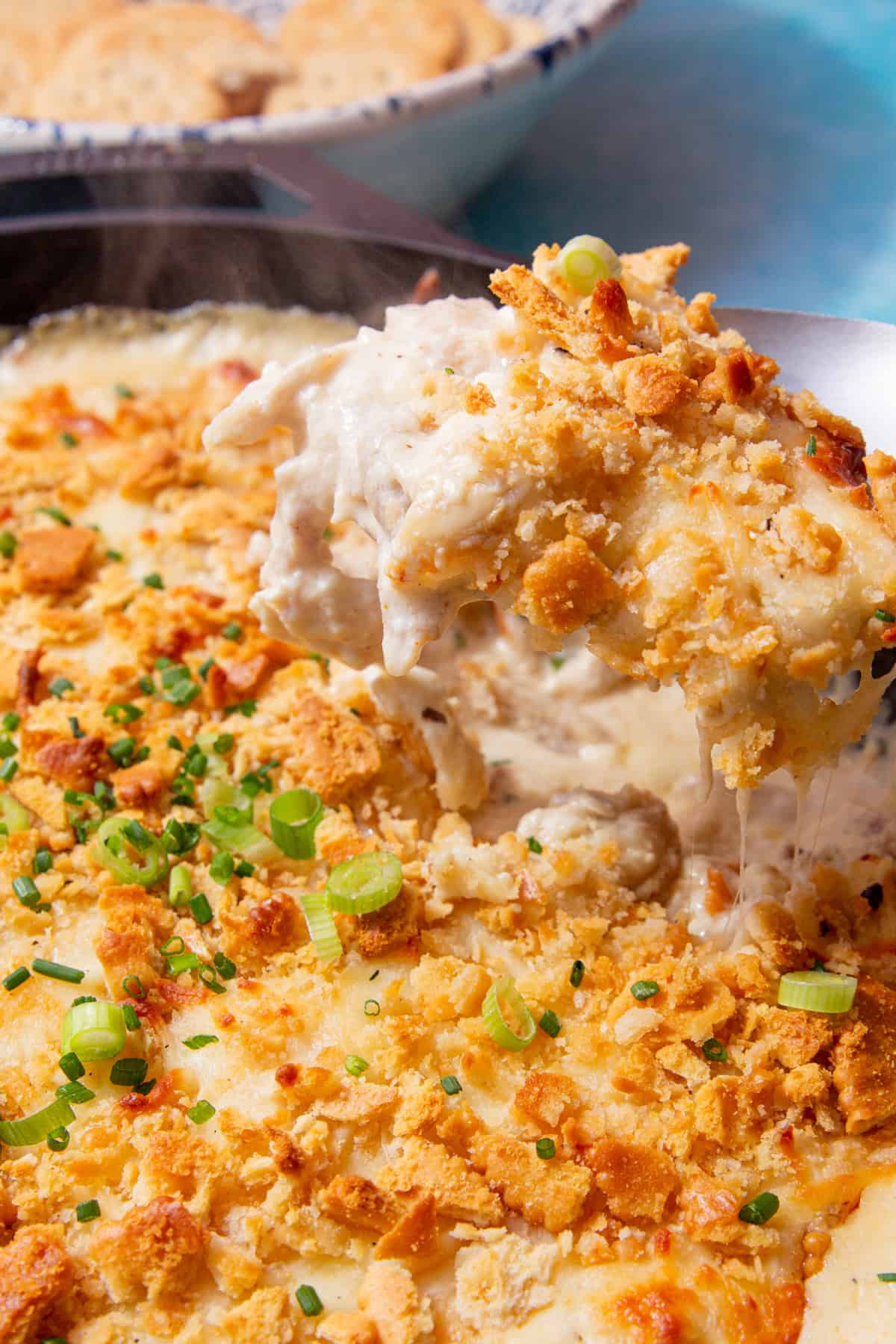 close up image of baked million dollar casserole in a black cast iron skillet being scooped out of the dish