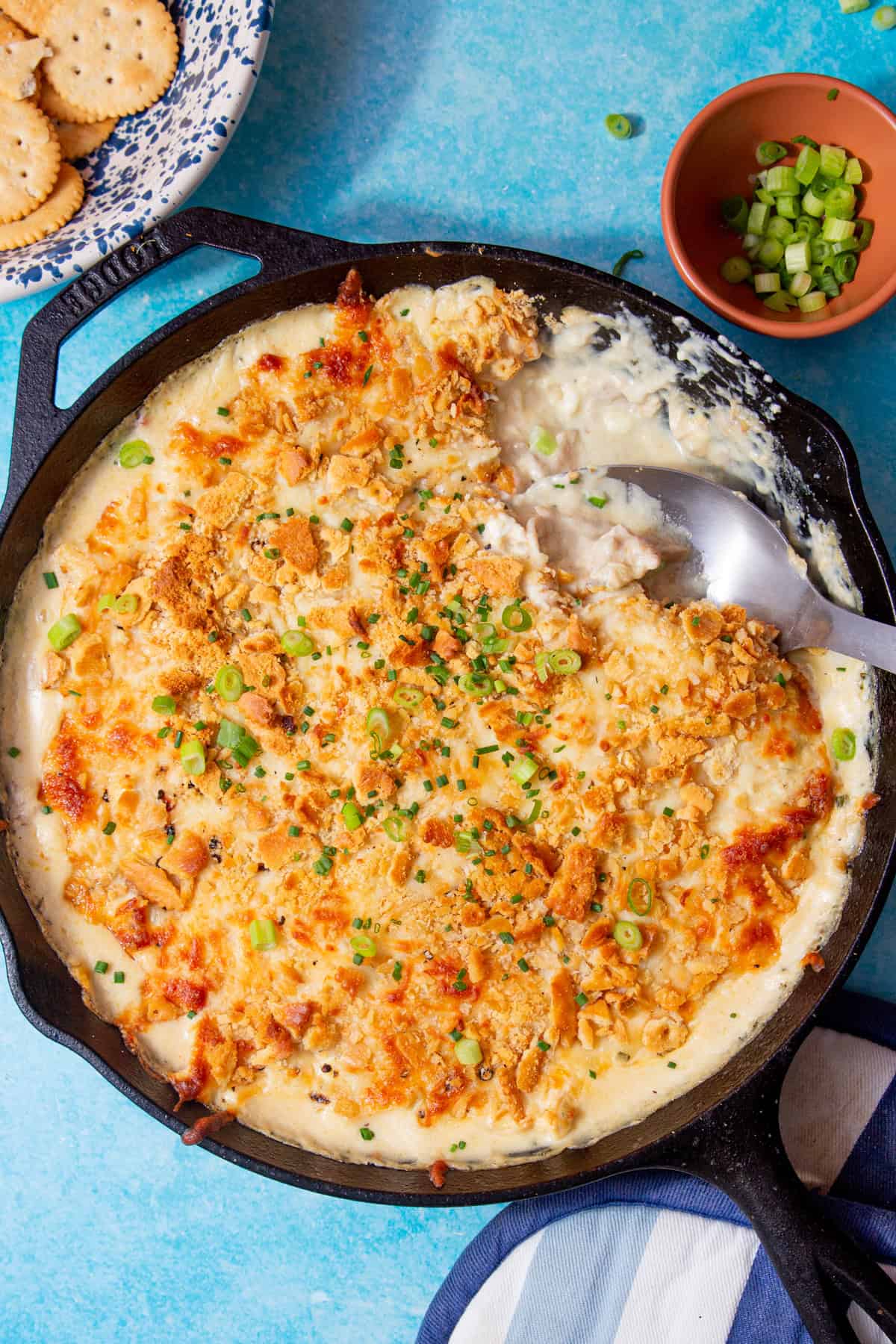 image of million dollar chicken casserole in a black skillet with a spoon in the dish on a blue background