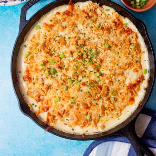 image of baked million dollar chicken casserole in a cast iron skillet on a blue background