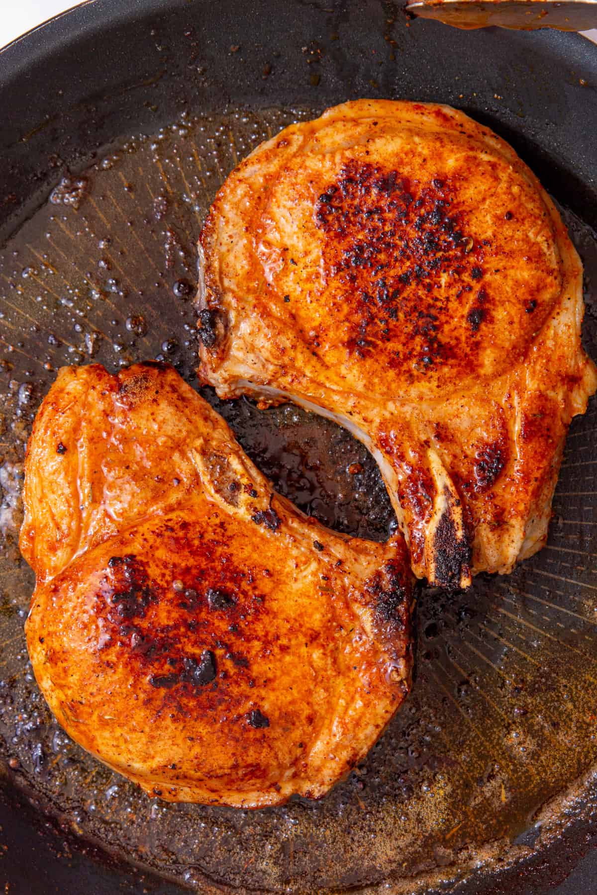 two fully cooked and caramelized pork chops with pork chop seasoning in a black skillet