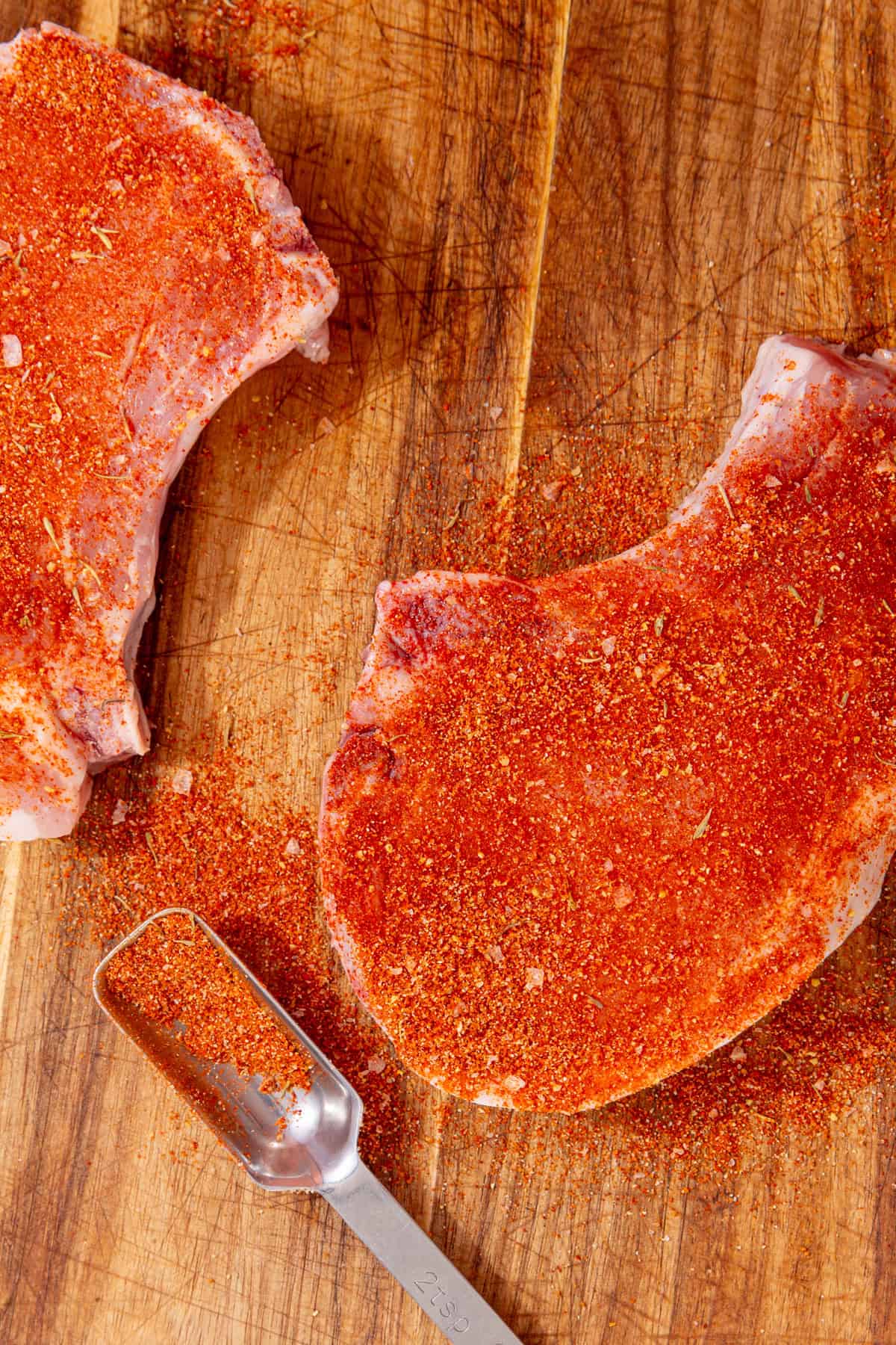 two pork chops covered with pork chop seasoning on a cutting board