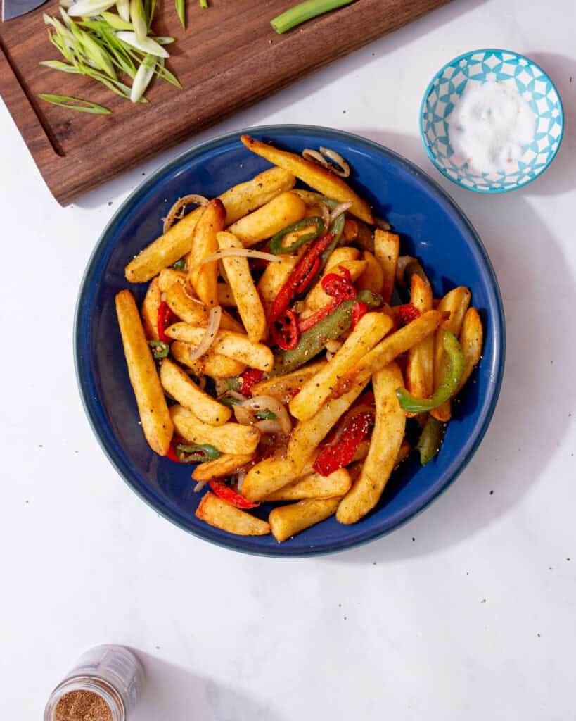 salt and pepper chips feature image containing chips with onions, peppers, salt and pepper in a blue bowl.