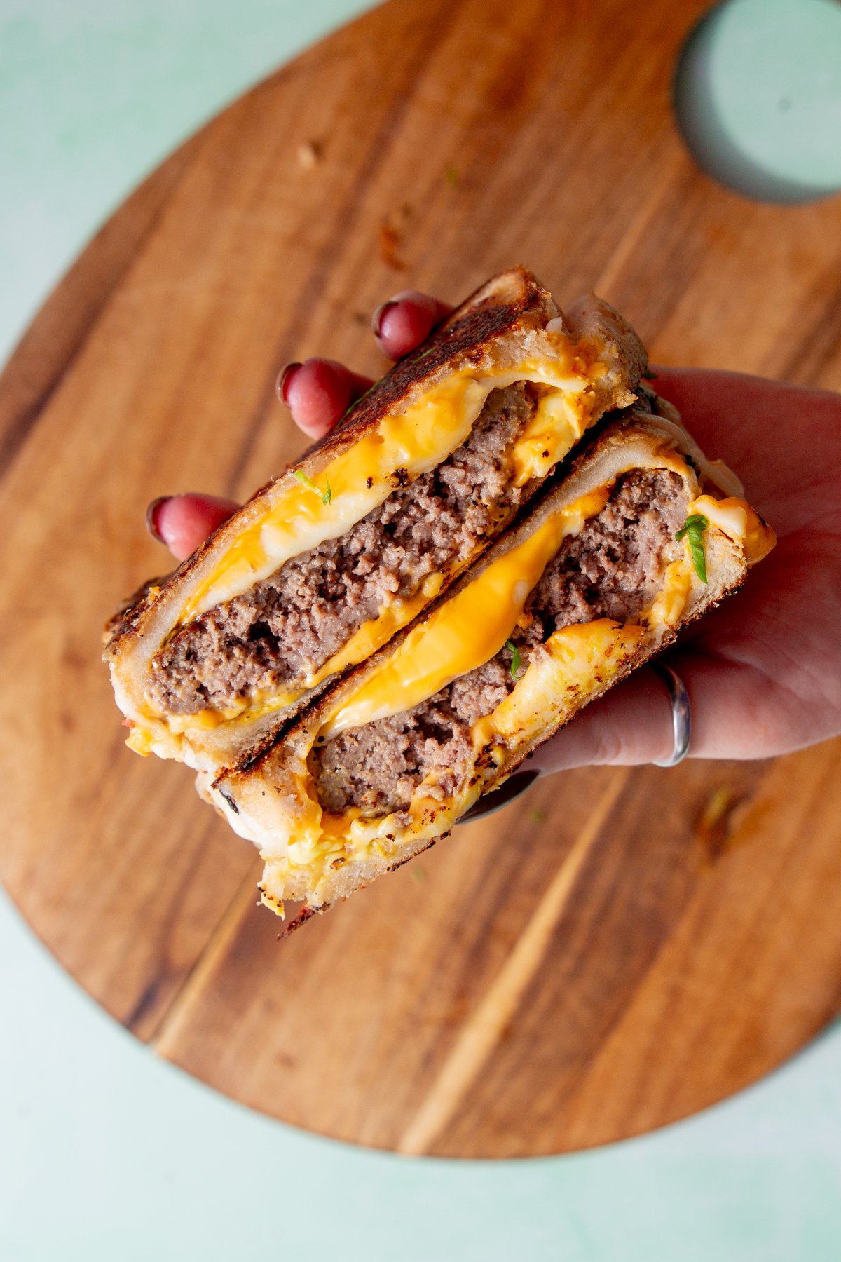 grilled cheese burger cut in half then stacked on top of one another and being held by a hand