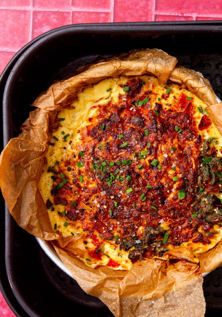 fully cooked air fryer frittata in an air fryer on a pink and white background