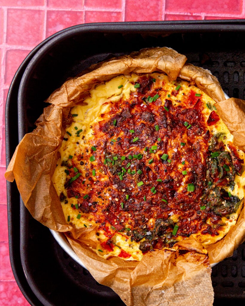 fully cooked air fryer frittata in an air fryer on a pink and white background