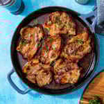 juicy, fully baked pork chops in a skillet that were baked in the oven and topped with fresh parsley all on a blue background