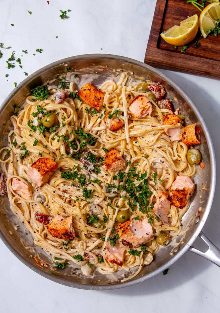 fully made salmon pasta dish in a skillet topped with fresh parsley and all on a grey-white background