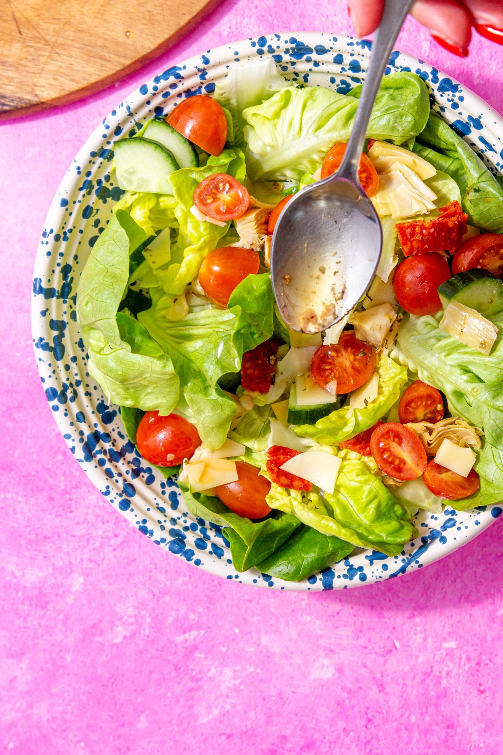 Up close image of submarine dressing being spooned onto a salad in a blue speckled bowl sitting on a pink background.