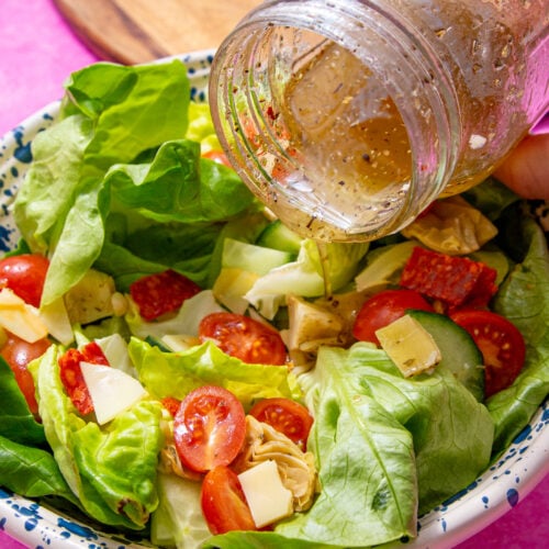 prepared homemade submarine dressing being poured over a salad form a mason jar.