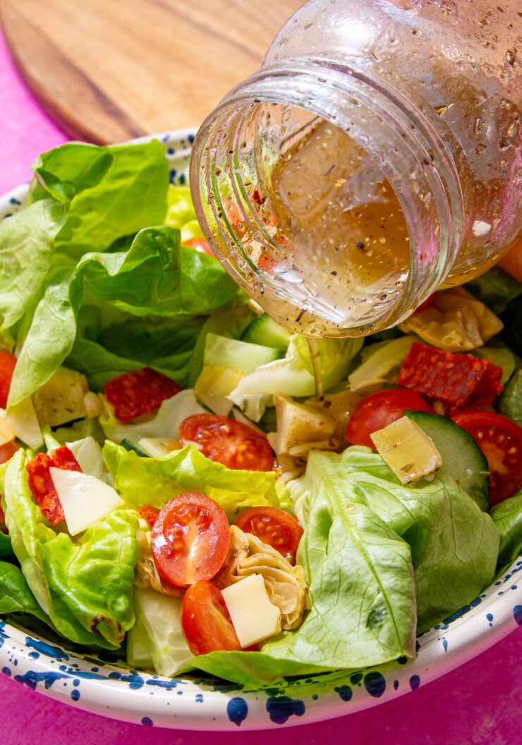 prepared homemade submarine dressing being poured over a salad form a mason jar.