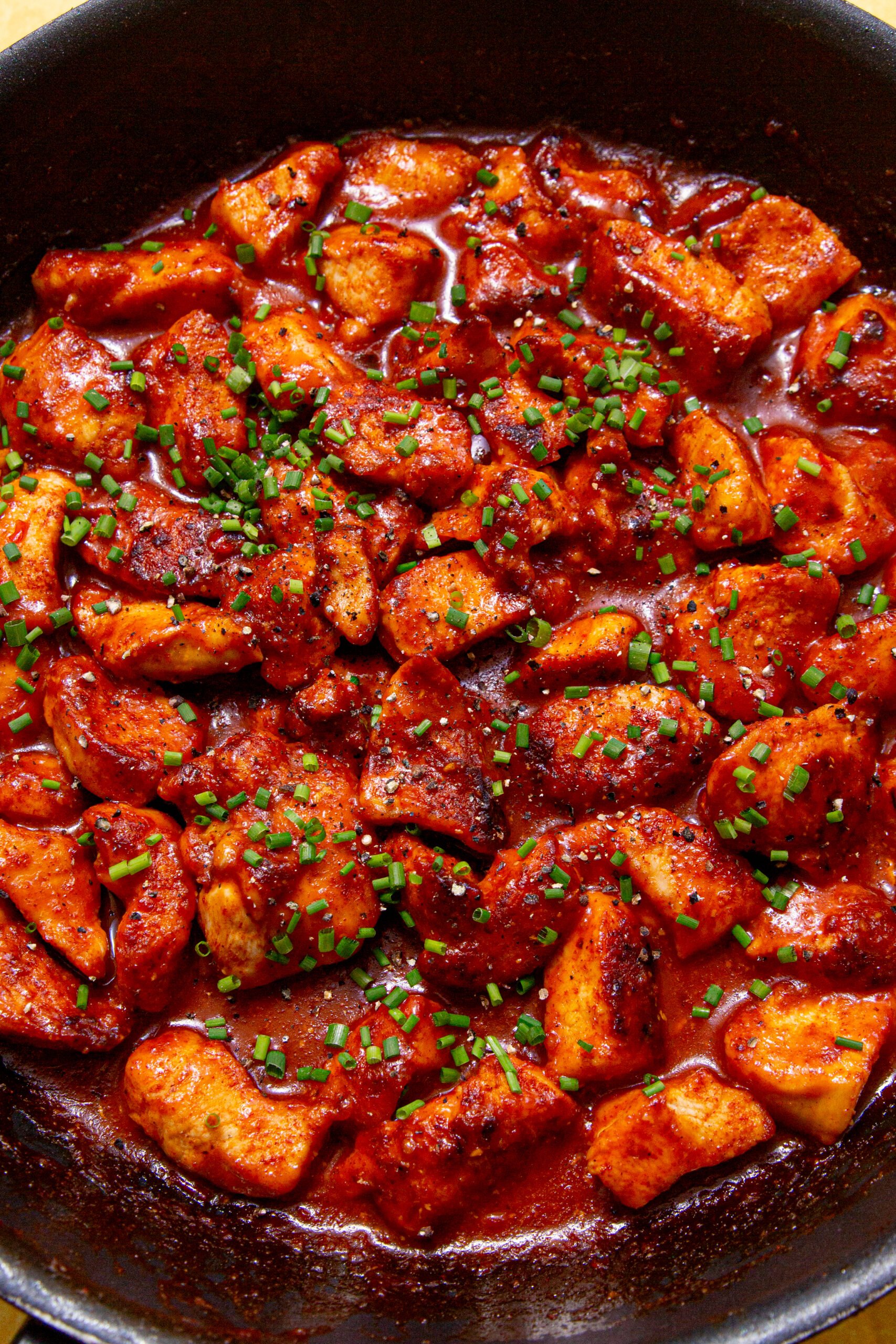 Close up image of sweet chilli chicken in a sticky sauce and topped with chives.