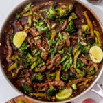 beef and broccoli recipe in a skillet on a white background and garnished with lime wedges