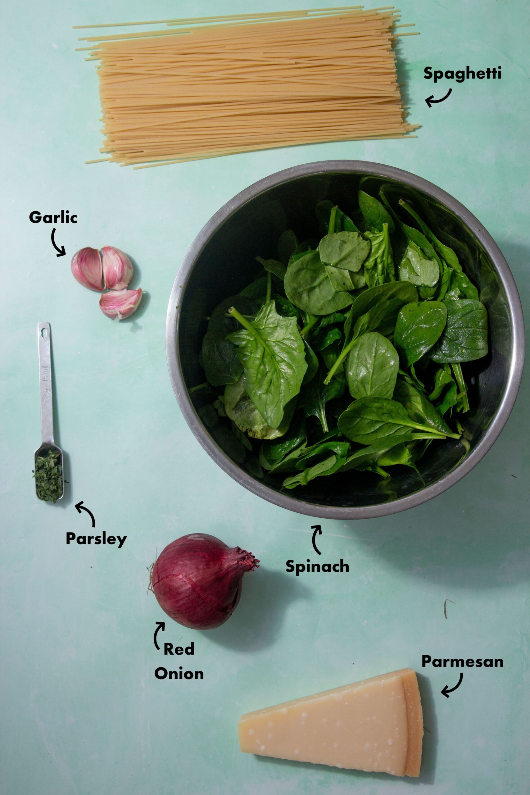 Ingredients to make the green spinach pasta sauce laid out on a pale blue background and labeled with arrows.