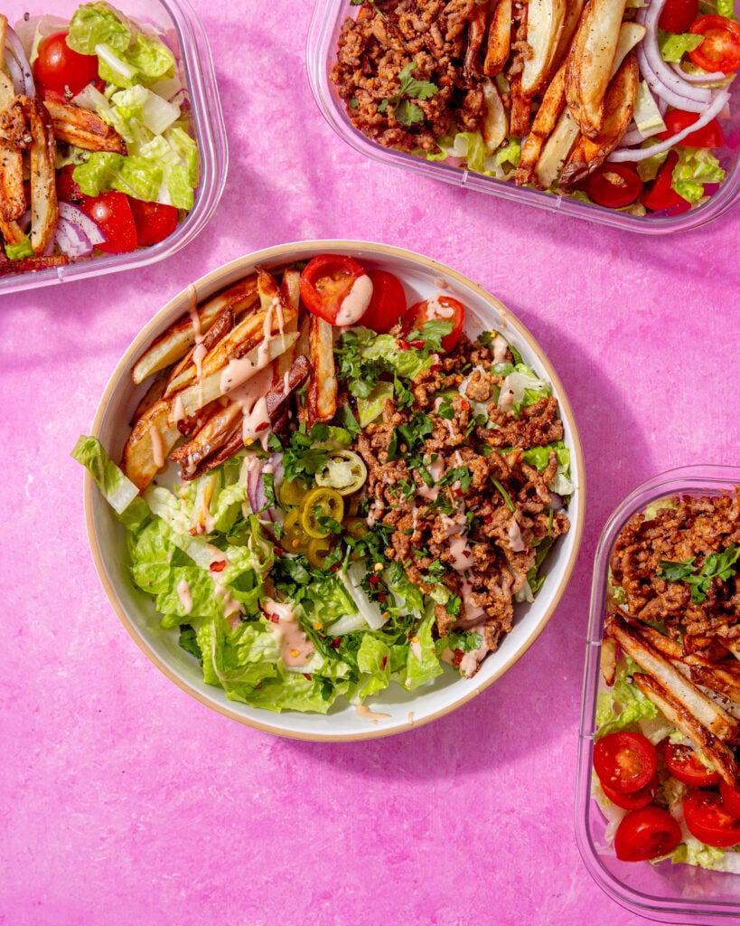 image of prepared burger bowl with other meal prep bowls around it on a pink background