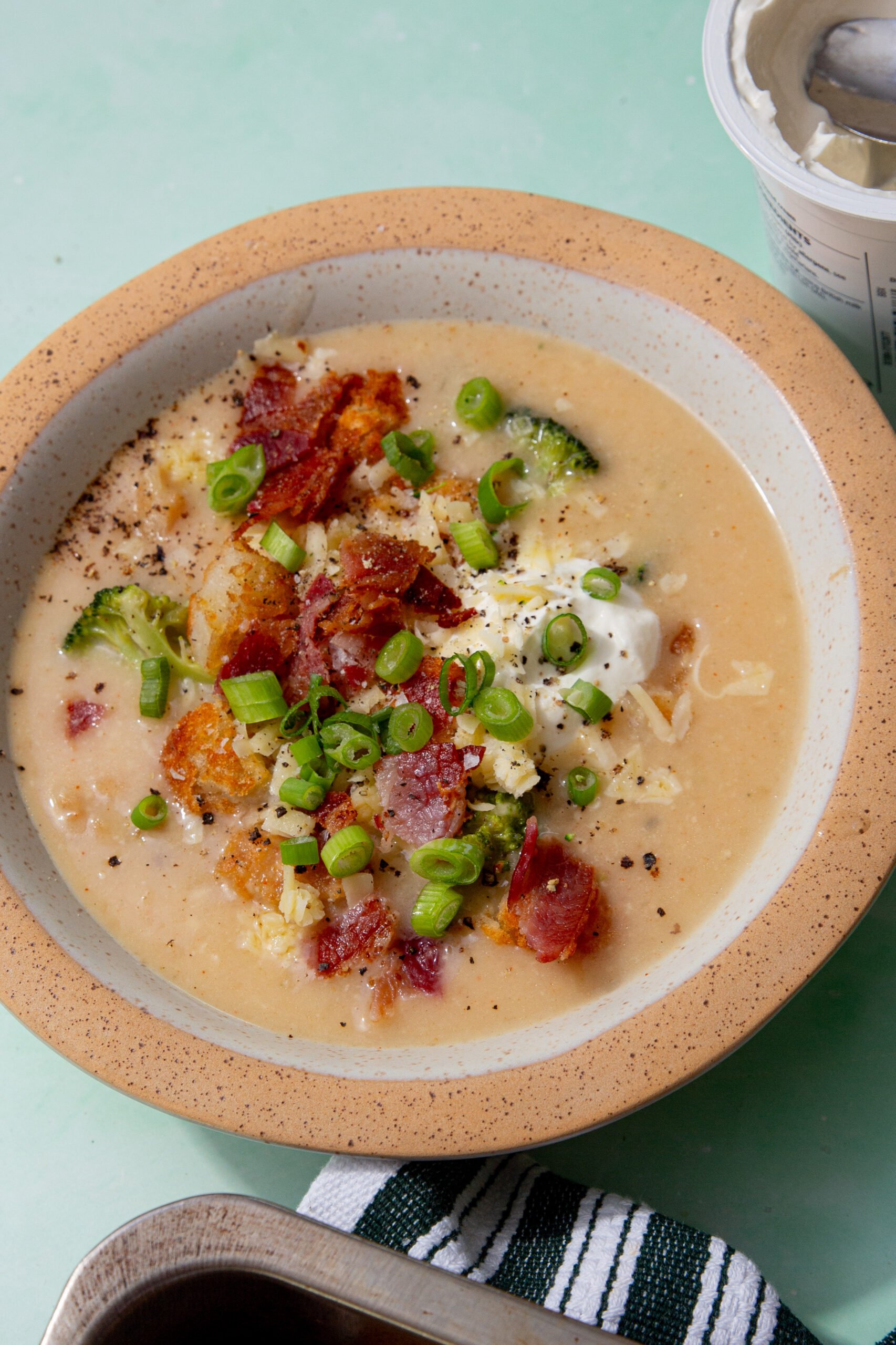 close up image of hash brown potato soup in a speckled bowl on a green background.