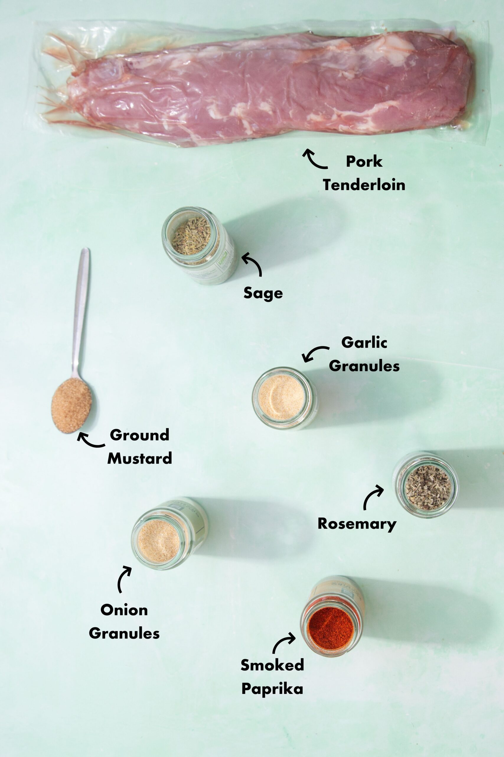 Ingredients to make the pork tenderloin in the oven laid out on a pale blue background and labeled with arrows.
