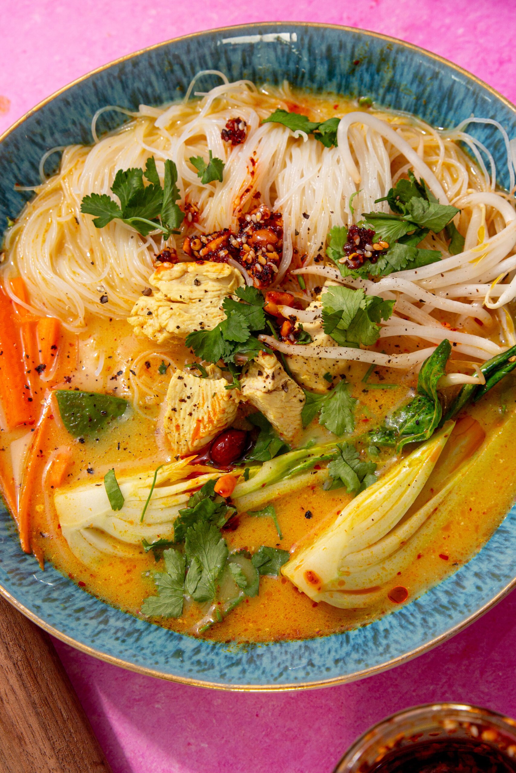 close up view of chicken laksa prepared in a blue bowl on a purple background