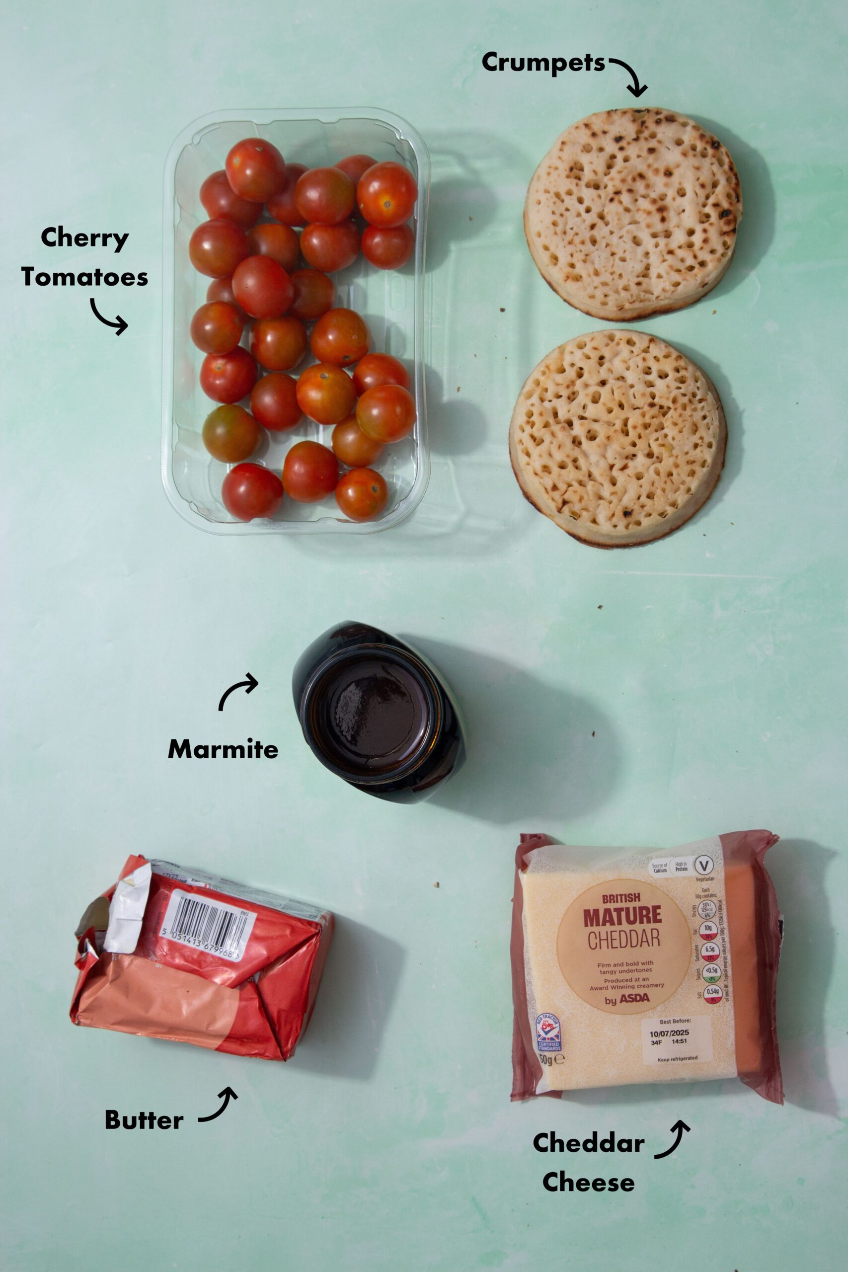 Ingredients to make the crumpets in the air fryer laid out on a pale blue background and labeled with arrows.
